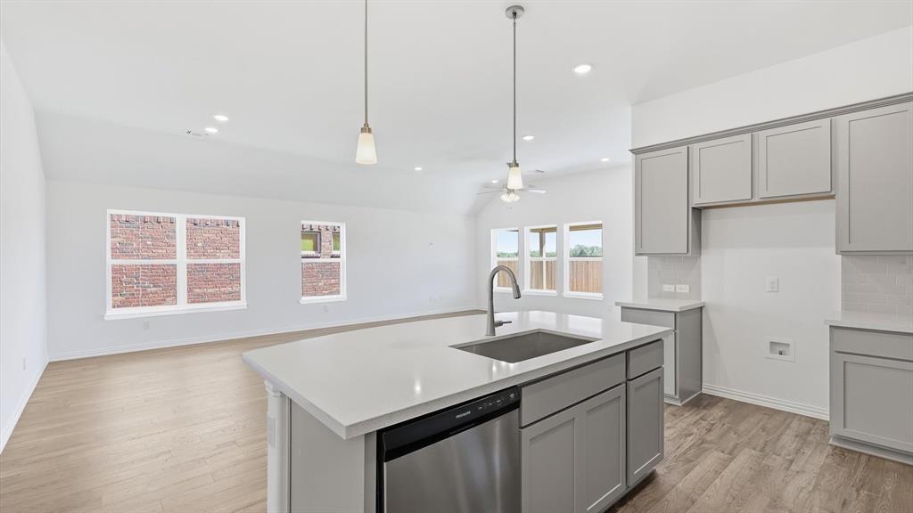 2529 Rivers W Road Anna, TX 75409 - Photo 21 of 40 Open-concept kitchen featuring a large island with sink, stainless steel dishwasher, pendant lighting, shaker-style cabinetry, and light-toned countertops