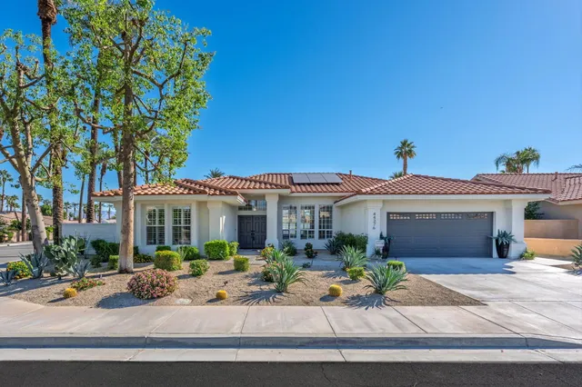 a view of a white house with large windows and a table and chairs under an umbrella