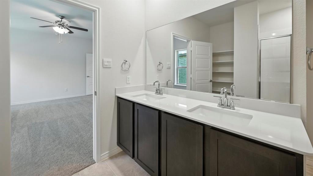412 Carthage Street Caddo Mills, TX 75135 - Photo 25 of 32 Bathroom vanity featuring dual undermount sinks with chrome faucets, a single large mirror, and dark wood-finish cabinetry
