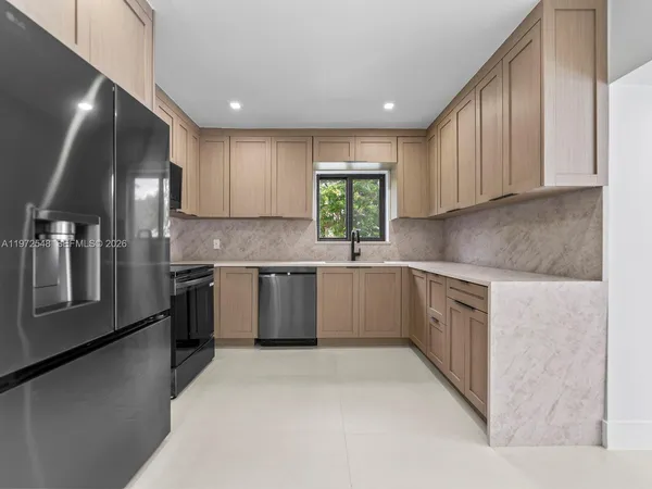 a kitchen with stainless steel appliances granite countertop a sink a stove a refrigerator cabinets and a window