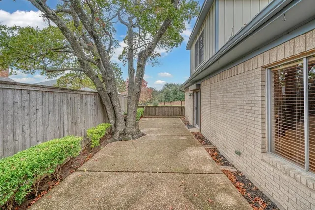 a view of a pathway with a white house with wooden fence and large trees