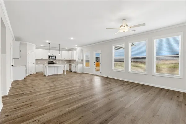 a view of an empty room with wooden floor and kitchen view