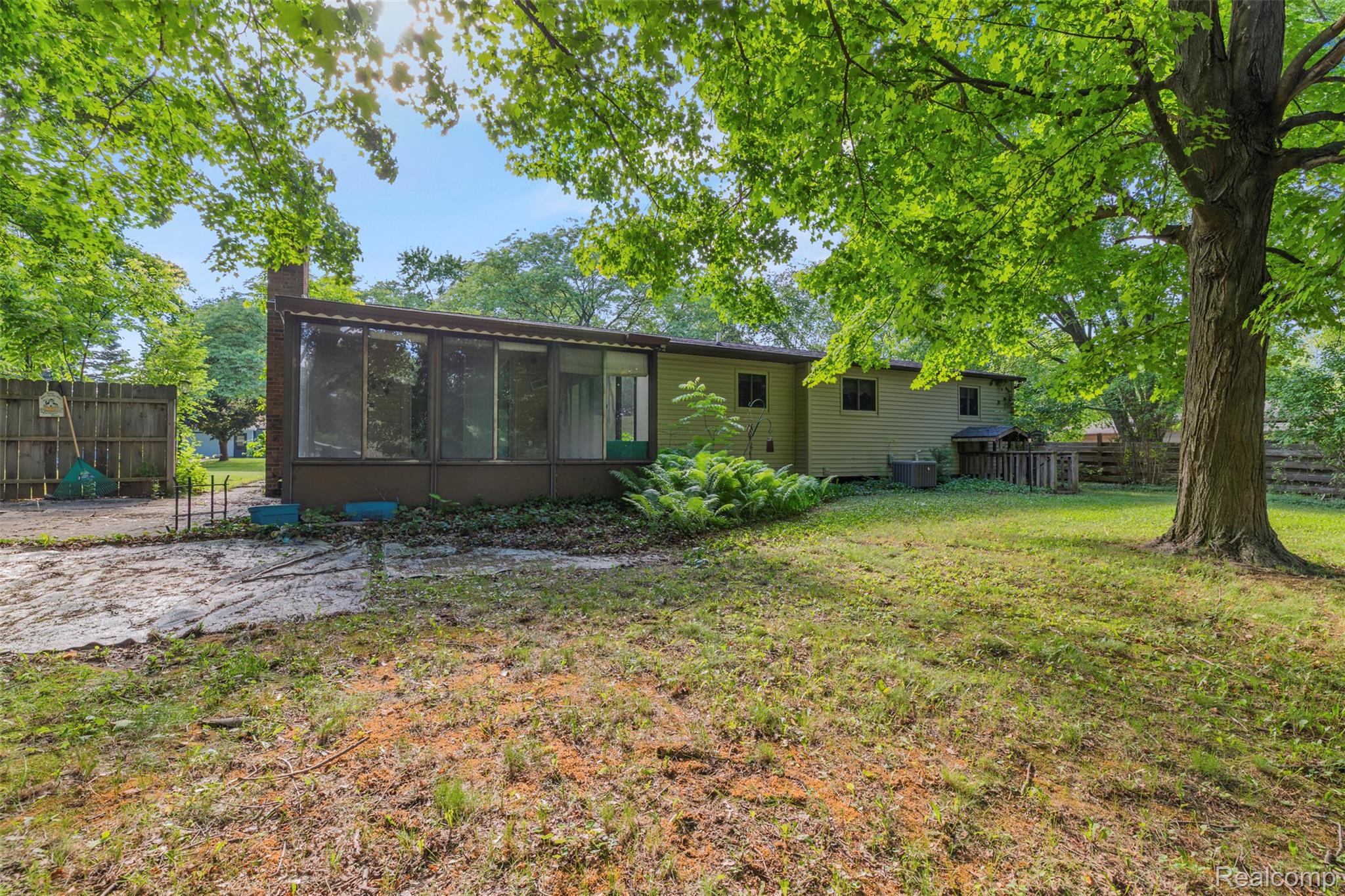 309 Windy Bluff Street Flushing, MI 48433 - Photo 28 of 32 Expansive backyard featuring a large sunroom with multiple windows, mature trees, and a wooden fence
