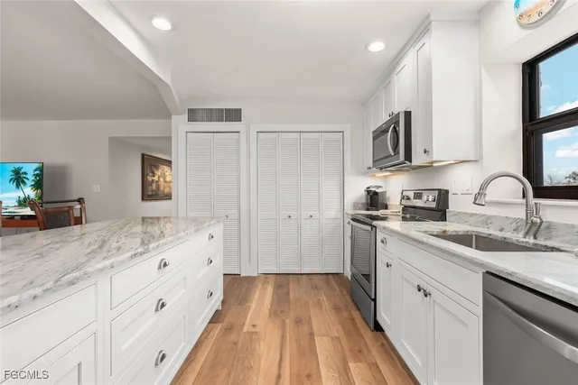 a kitchen with a sink dishwasher and white cabinets with wooden floor