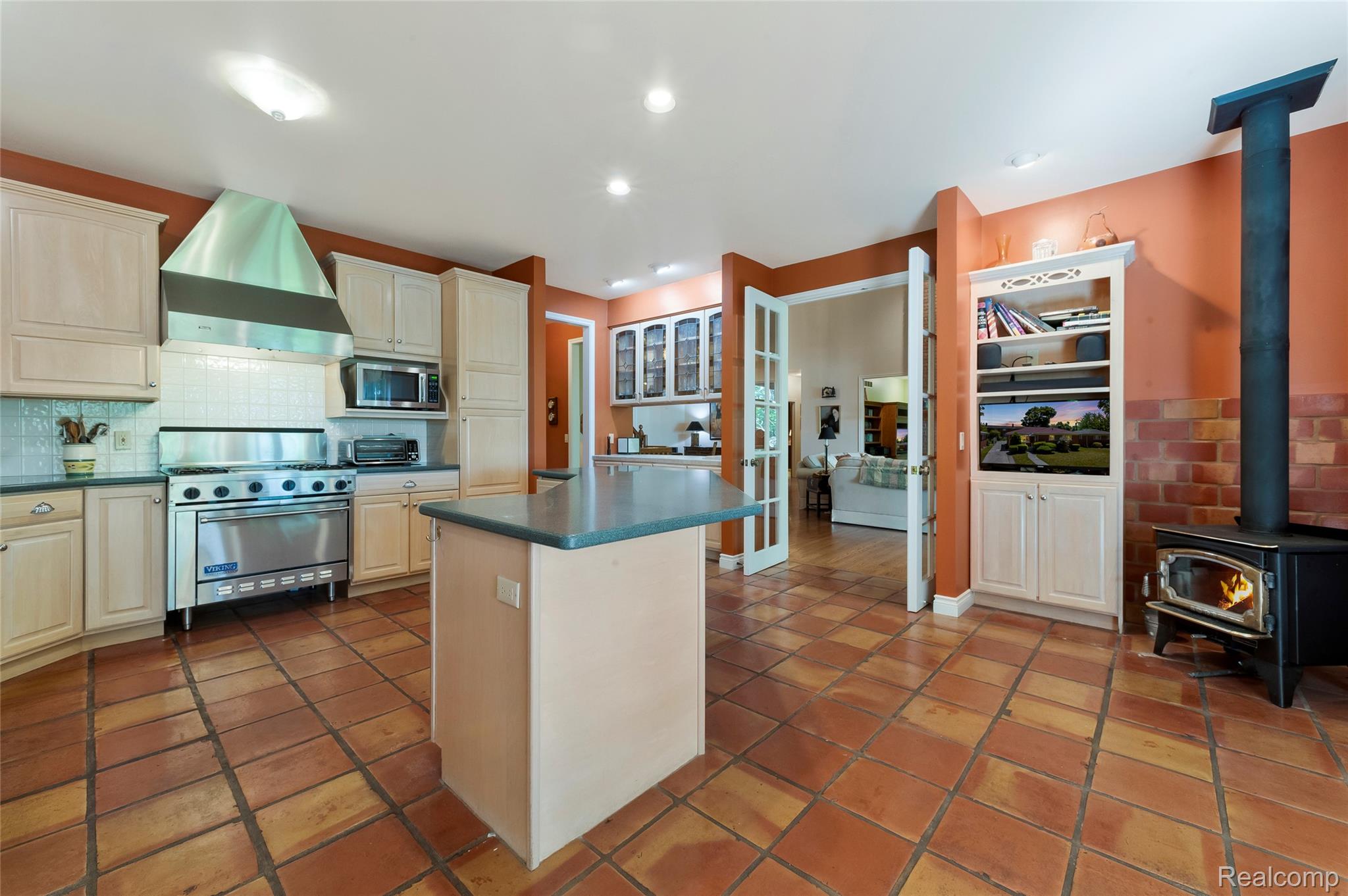 2323 Addaleen Road Highland, MI 48357 - Photo 36 of 70 Spacious kitchen featuring terracotta tile flooring, light wood cabinetry, a central island, professional-grade stainless steel appliances and a wood burning stove