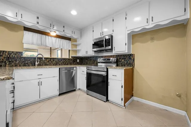 a kitchen with stainless steel appliances granite countertop a stove a sink and white cabinets