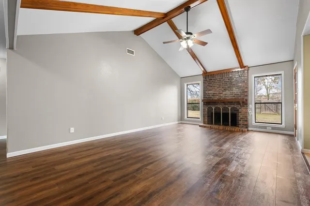a view of an empty room with wooden floor fireplace and a window