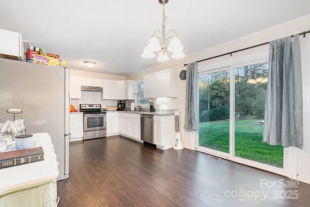 a open kitchen with stainless steel appliances granite countertop a stove a refrigerator a oven with white cabinets and wooden floor