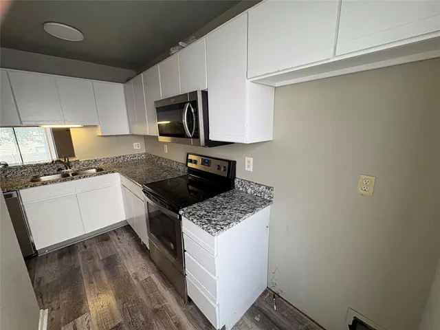 a kitchen with granite countertop a sink a stove top oven and cabinetry