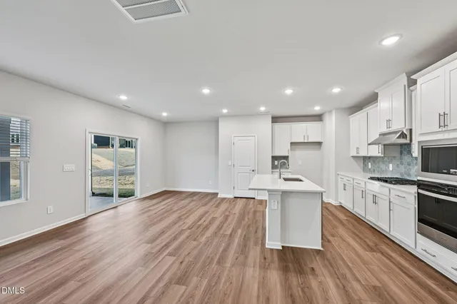 a kitchen with stainless steel appliances granite countertop a stove top oven a sink dishwasher and a refrigerator with wooden floor