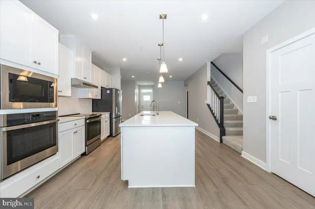 a kitchen with a sink stainless steel appliances and wooden floor