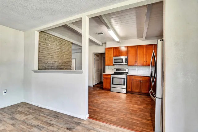 a kitchen with stainless steel appliances kitchen island granite countertop a refrigerator a stove and a wooden floors