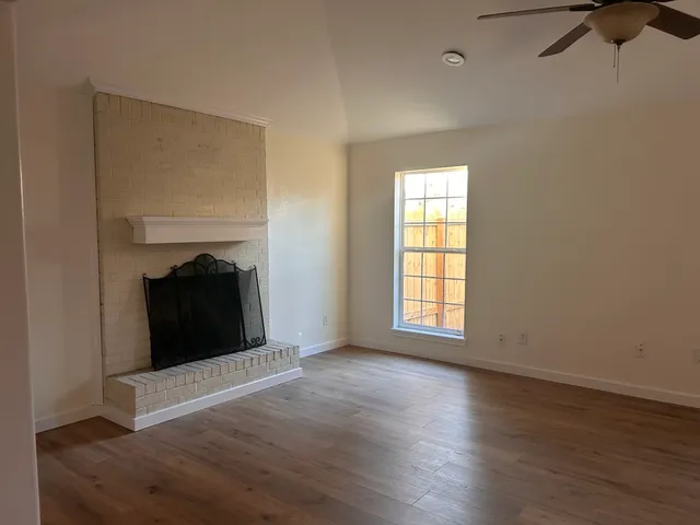 an empty room with wooden floor fireplace and windows