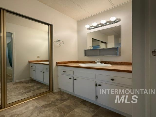 1360 Pioneer Road Weiser, ID 83672 - Photo 20 of 47 Bathroom featuring a vanity with a white basin sink and wood-finish countertop, white base cabinetry with dark hardware, a wall-mounted mirror with integrated lighting, and tile flooring