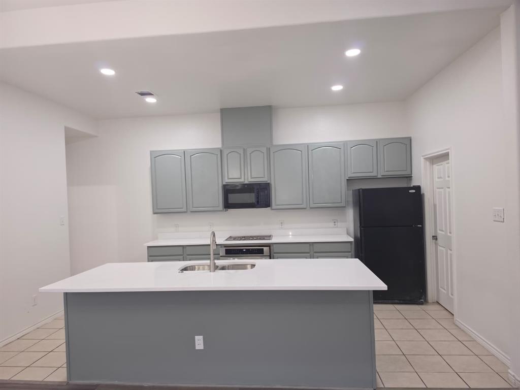 8047 New Kent Road Frisco, TX 75035 - Photo 8 of 27 Kitchen featuring a central island with a stainless steel sink, solid surface countertops, light gray cabinetry, and recessed lighting