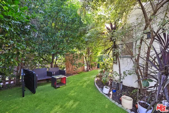 a backyard of a house with table and chairs potted plants and large tree