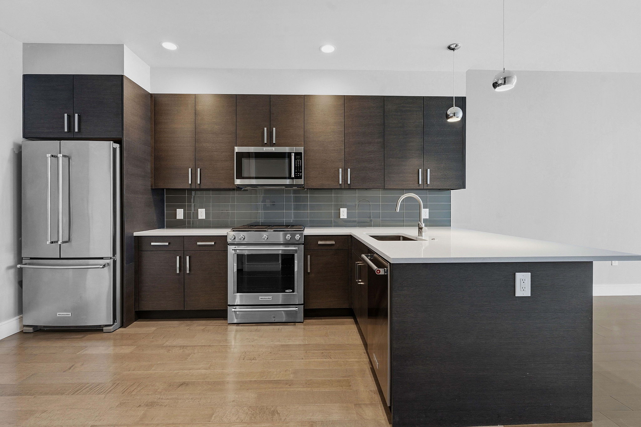 222 West Avenue, Unit 2207 Austin, TX 78701 - Photo 3 of 30 Contemporary kitchen featuring a full suite of stainless steel appliances, dark wood-finish cabinetry, light-toned countertops, and a gray subway tile backsplash
