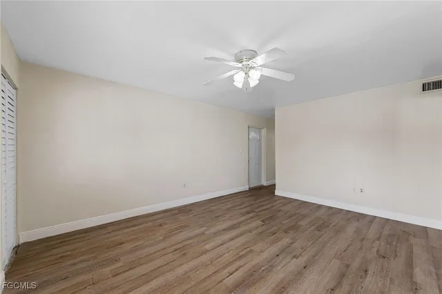 a view of an empty room with wooden floor and a ceiling fan