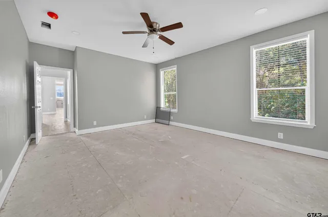 an empty room with ceiling fan and windows