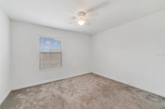 an empty room with chandelier fan and windows
