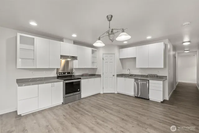 a large kitchen with stainless steel appliances granite countertop a stove top oven a sink dishwasher a refrigerator and white cabinets with wooden floor