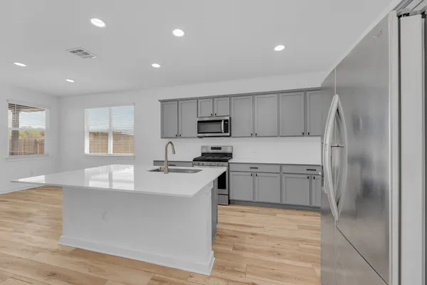 a kitchen with stainless steel appliances a refrigerator stove a sink and white cabinets with wooden floor