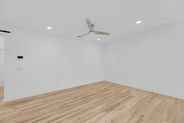 a view of an empty room with wooden floor and a ceiling fan
