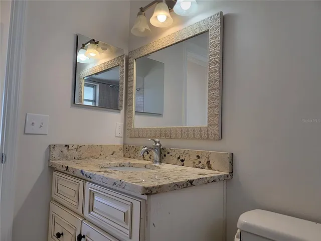 a bathroom with a granite countertop sink a toilet and mirror