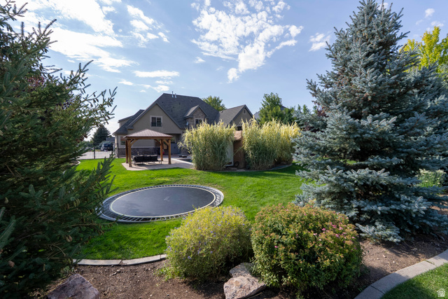 687 South 2080th Street East Springville, UT 84663 - Photo 110 of 149 Spacious backyard featuring an in-ground trampoline, a covered gazebo on a paved patio, and mature trees and shrubs