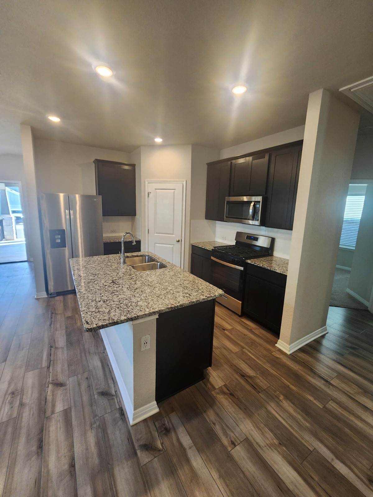 623 Sungrove Trail Georgetown, TX 78628 - Photo 3 of 17 Kitchen with stainless steel appliances, light stone counters, a center island with sink, dark wood-style flooring, and recessed lighting