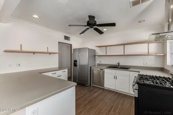a kitchen with stainless steel appliances granite countertop a refrigerator a sink dishwasher a stove and white countertops with wooden floor