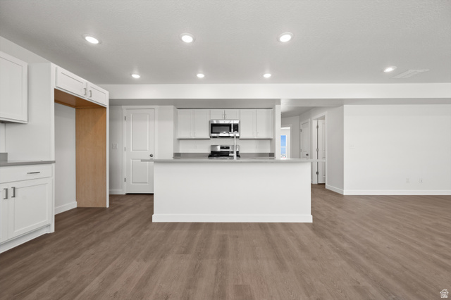 1554 Pheasant Road Eagle Mountain, UT 84005 - Photo 8 of 29 Kitchen with white cabinetry, stainless steel appliances, a center island with sink, light countertops, and dark wood-style flooring