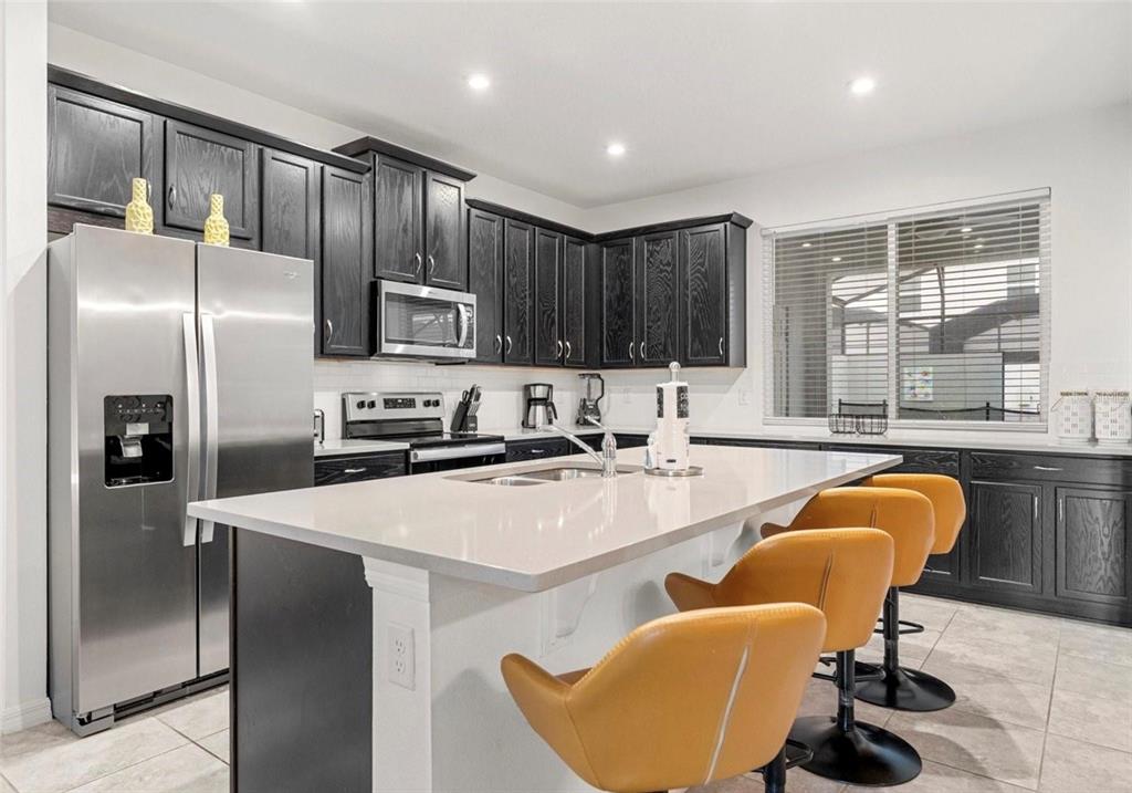 2163 Copper Bell Place Kissimmee, FL 34747 - Photo 15 of 41 a kitchen with stainless steel appliances granite countertop a refrigerator a stove a sink a dining table and chairs with wooden floor