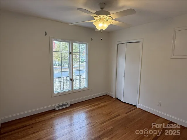 an empty room with wooden floor chandelier fan and windows