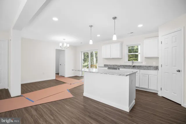 a view of an empty room with wooden floor and a kitchen