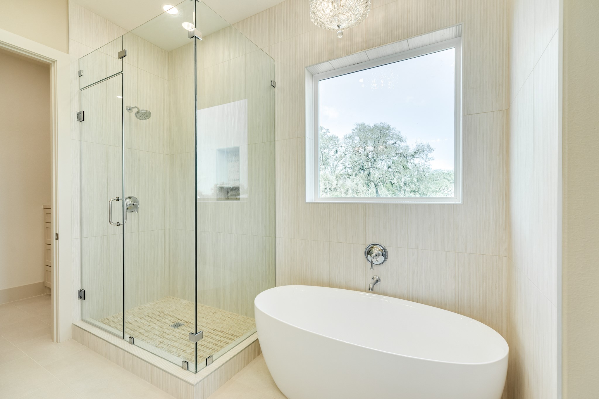 1737 Flintlock Court Angleton, TX 77515 - Photo 27 of 47 This bathroom features a modern glass-enclosed shower and a sleek freestanding tub. Natural light pours in through a large window, highlighting the elegant tile work and creating a serene, spa-like atmosphere.