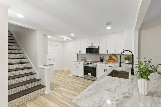 a large white kitchen with wooden floor and stainless steel appliances