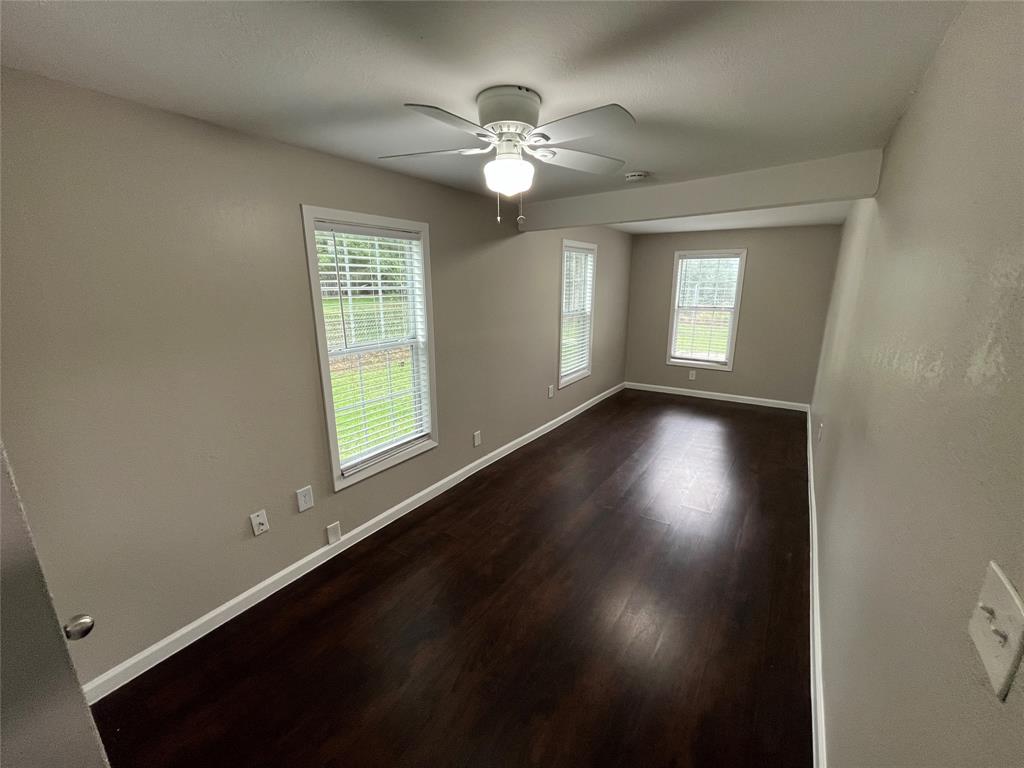 9558 Rylie Crest Drive Dallas, TX 75217 - Photo 11 of 14 Spacious room featuring dark wood-finish flooring, neutral wall tones, white trim, multiple windows with blinds, and a ceiling fan with integrated lighting