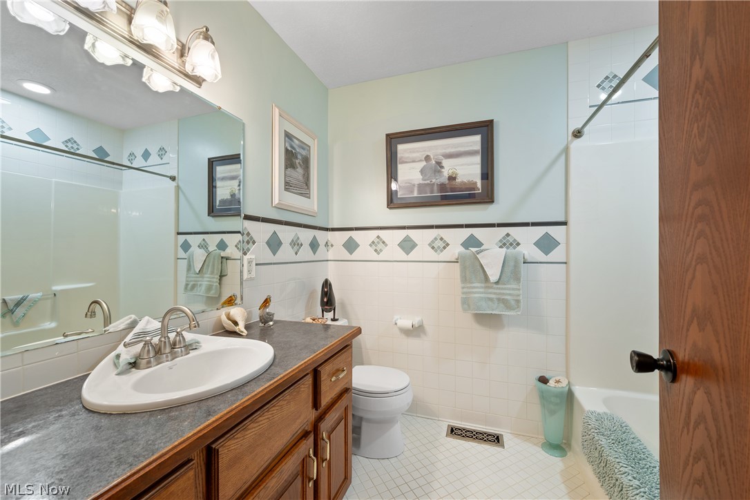 10400 Stoneacre Road Northwest Canal Fulton, OH 44614 - Photo 21 of 44 Bathroom with vanity, tile walls, tile patterned floors, shower / bathtub combination, and wainscoting