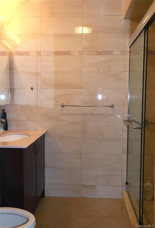 71-38 147th Street, Unit 27A Queens, NY 11367 - Photo 7 of 8 Full bath featuring vanity, a shower stall, tile walls, and tile patterned flooring