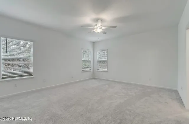 an empty room with chandelier fan and windows