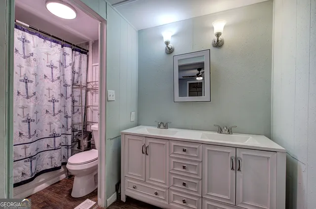 a bathroom with a granite countertop toilet a sink a mirror a window and vanity