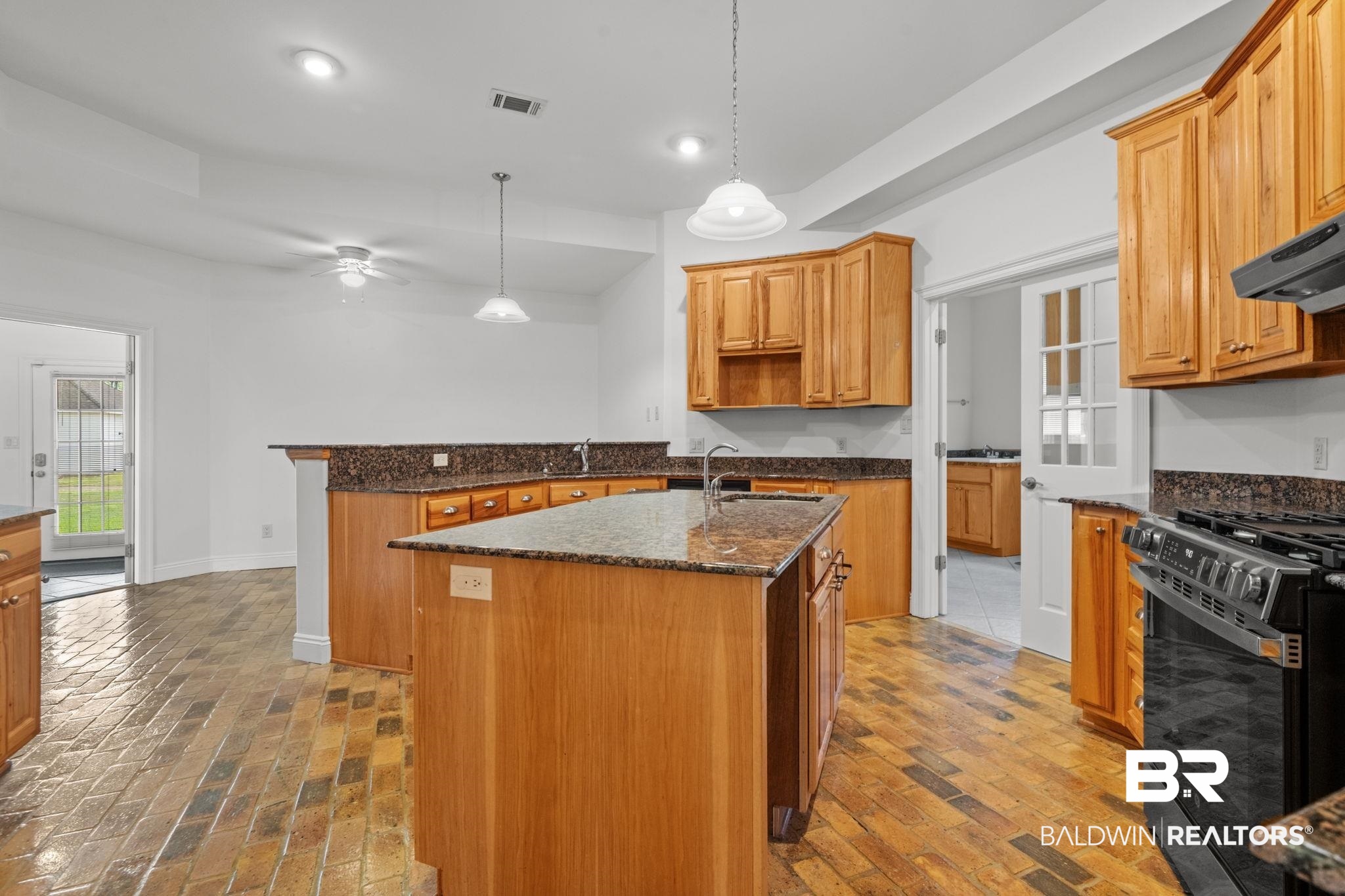 29634 St George Street Daphne, AL 36526 - Photo 18 of 47 Kitchen with a kitchen island with sink, dark stone countertops, black range with gas cooktop, pendant lighting, and a peninsula