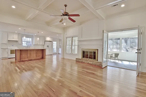 an empty room with wooden floor a fireplace a kitchen view and a window