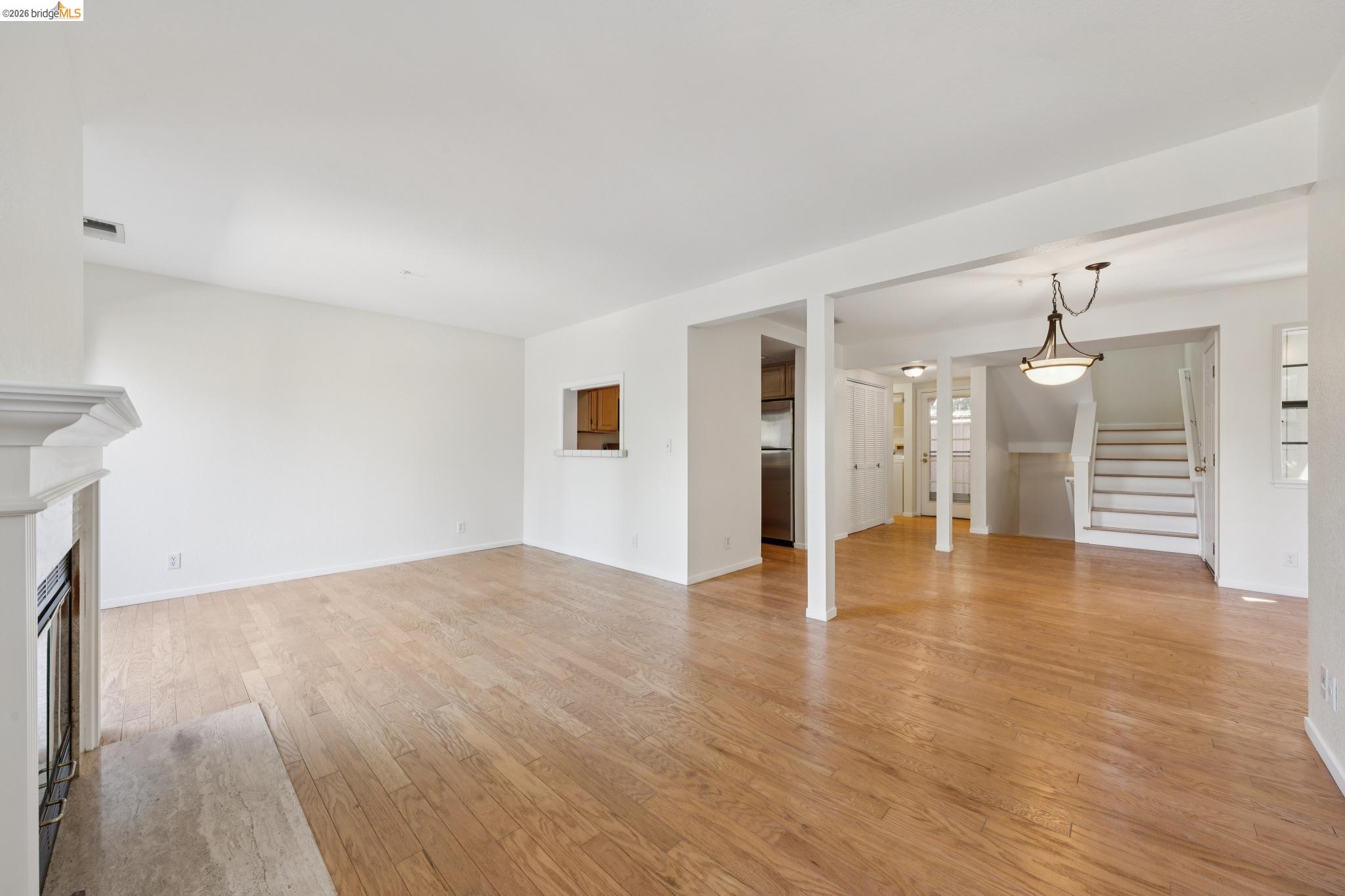 261 Redhawk Road Novato, CA 94949 - Photo 14 of 44 Expansive living area featuring wood-finish flooring, a white mantel fireplace with a stone hearth, and a pass-through window with wood cabinetry