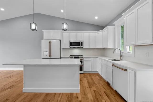 a kitchen with stainless steel appliances granite countertop a sink a stove top oven a refrigerator with white cabinets and wooden floor