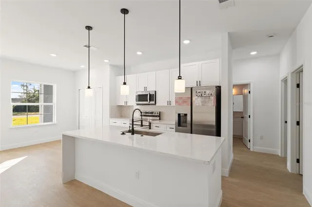 a kitchen with stainless steel appliances kitchen island granite countertop a refrigerator a sink and white cabinets