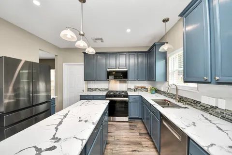 a large kitchen with a large counter top space a sink stainless steel appliances and cabinets