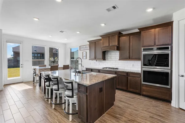 a large kitchen with kitchen island granite countertop a stove top oven a sink a dining table and chairs with wooden floor