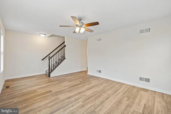 a view of an empty room with wooden floor and a ceiling fan